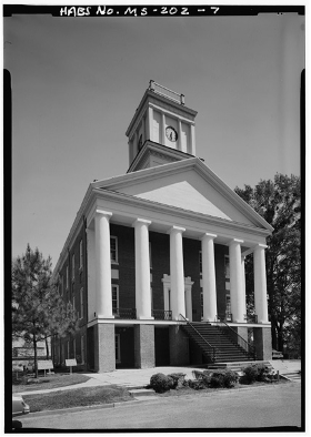 Black and white photograph of a facade of a three-story building constructed in a Greek Revival-style on the campus of Alcorn University with trees in the background.